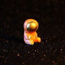 A little hand-sculpted sitting astronaut on a black starry background.
